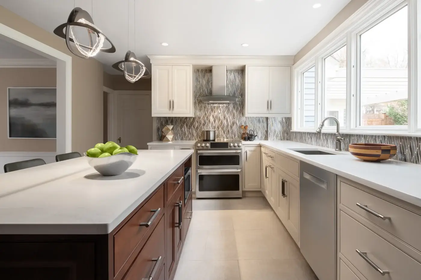 Spacious kitchen with white and brown cabinetry, stainless steel appliances, granite backsplash, two pendant lights, and large windows overlooking a backyard.