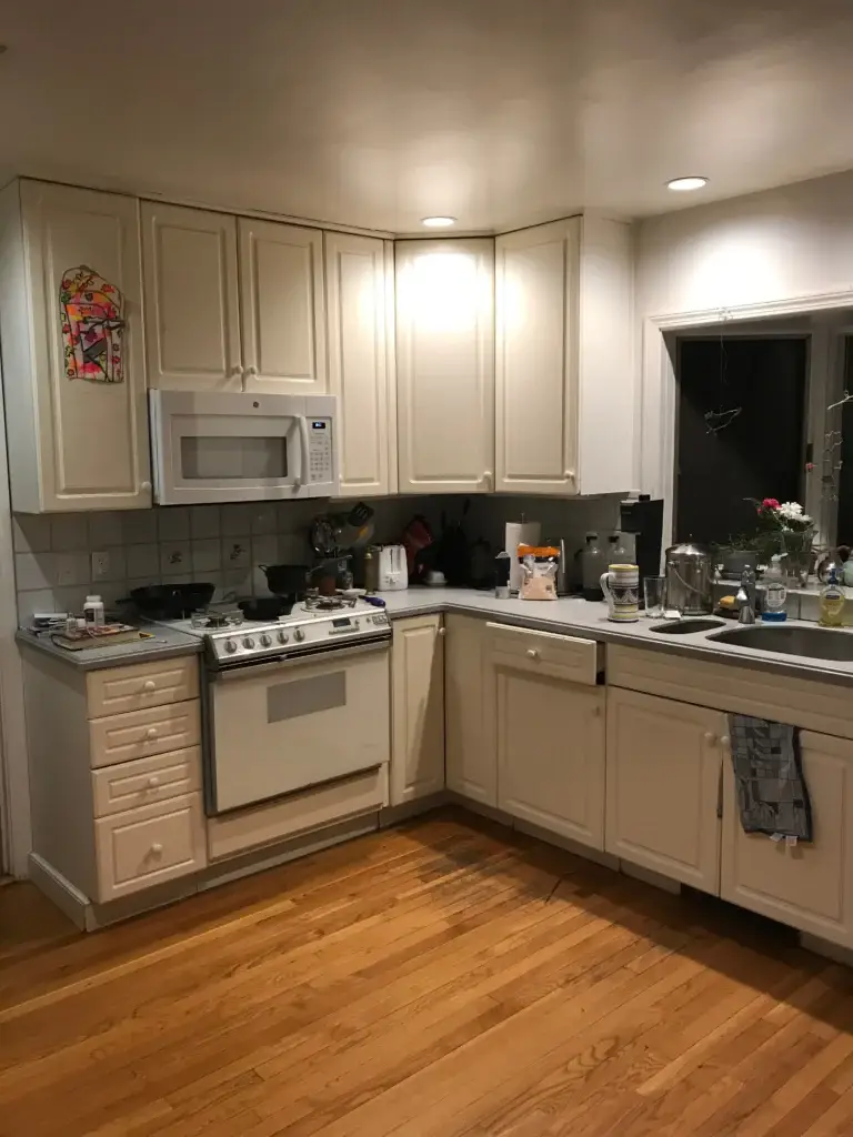 A kitchen with cream-colored cabinets, stainless steel appliances, dark countertops, wood flooring, and recessed lighting throughout.