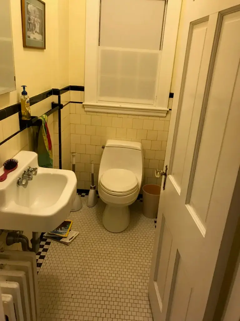 A small bathroom with pale yellow walls, white subway tile, a pedestal sink on the left, a toilet in the center, and cream-colored doors on the right.