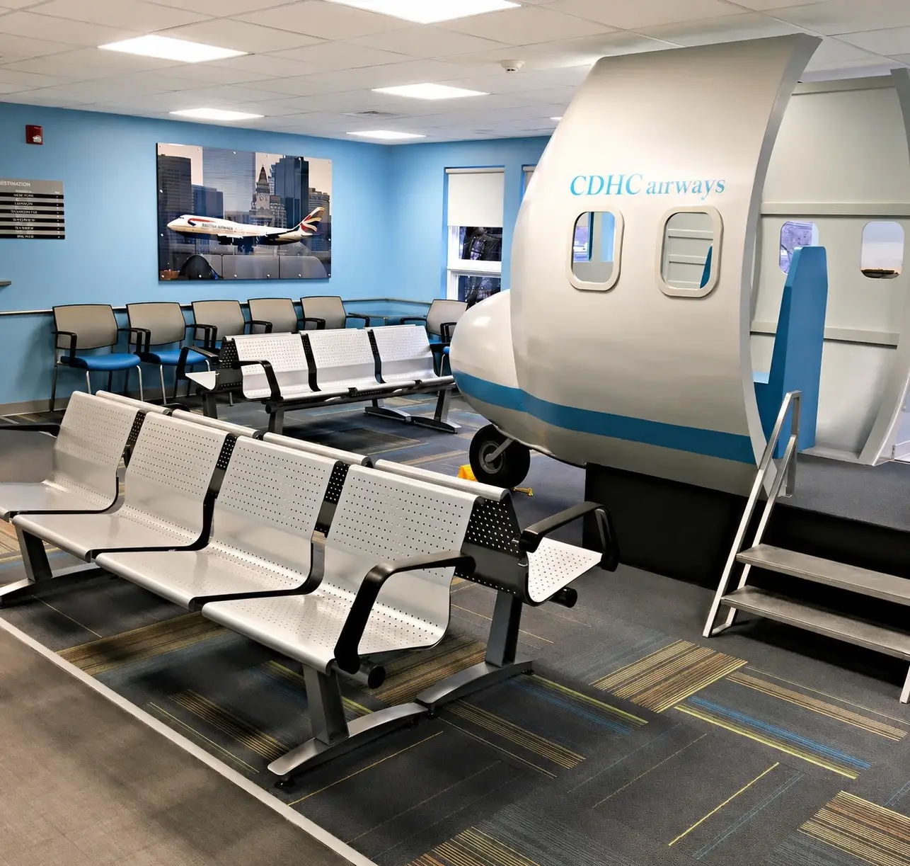 Indoor training facility with white and blue aircraft fuselage mock-up labeled CDHC airways next to waiting area seating.
